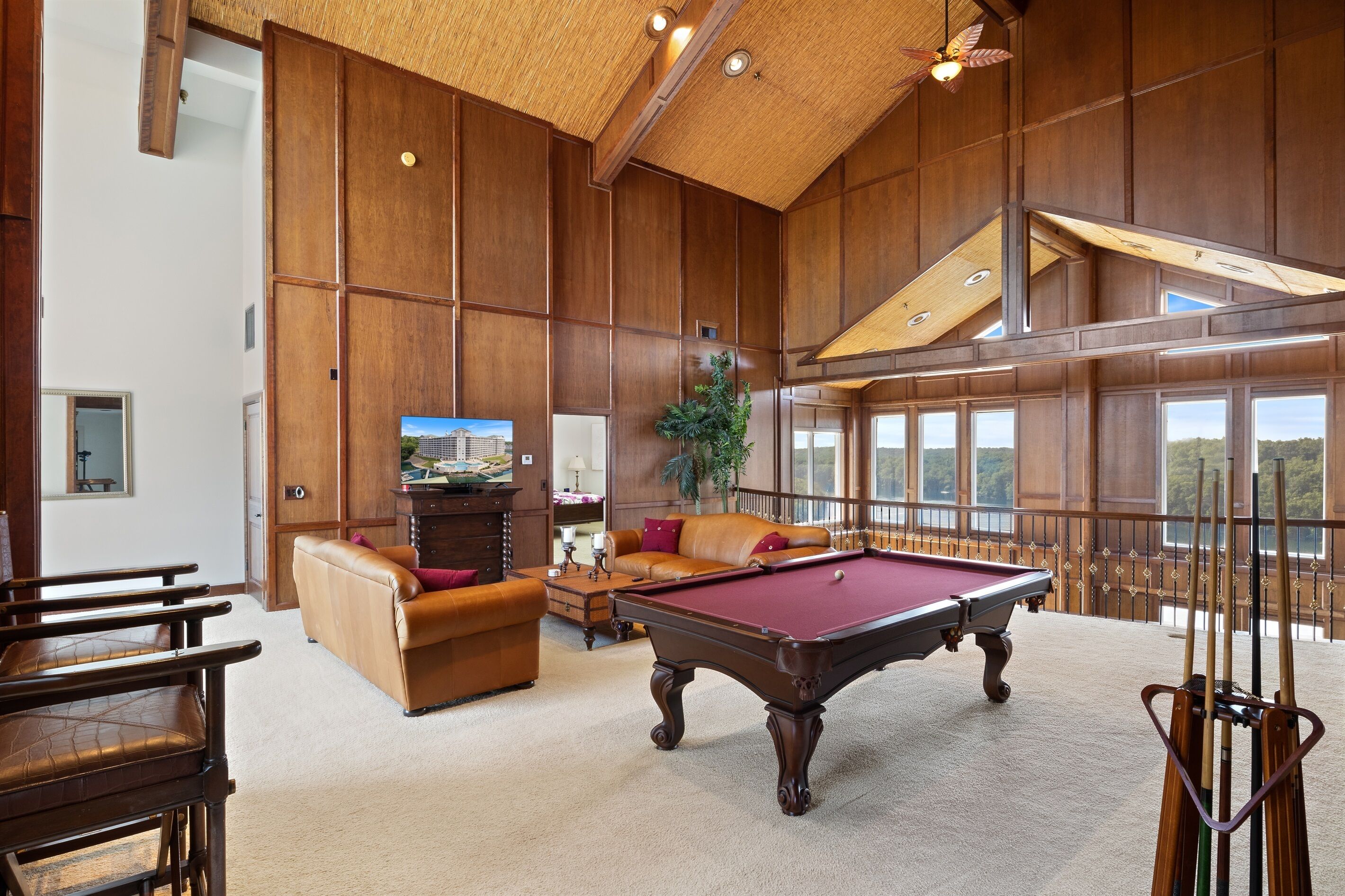 Une pièce spacieuse équipée d’une table de billard, d’un canapé en cuir et d’une grande fenêtre donnant sur un paysage agréable.