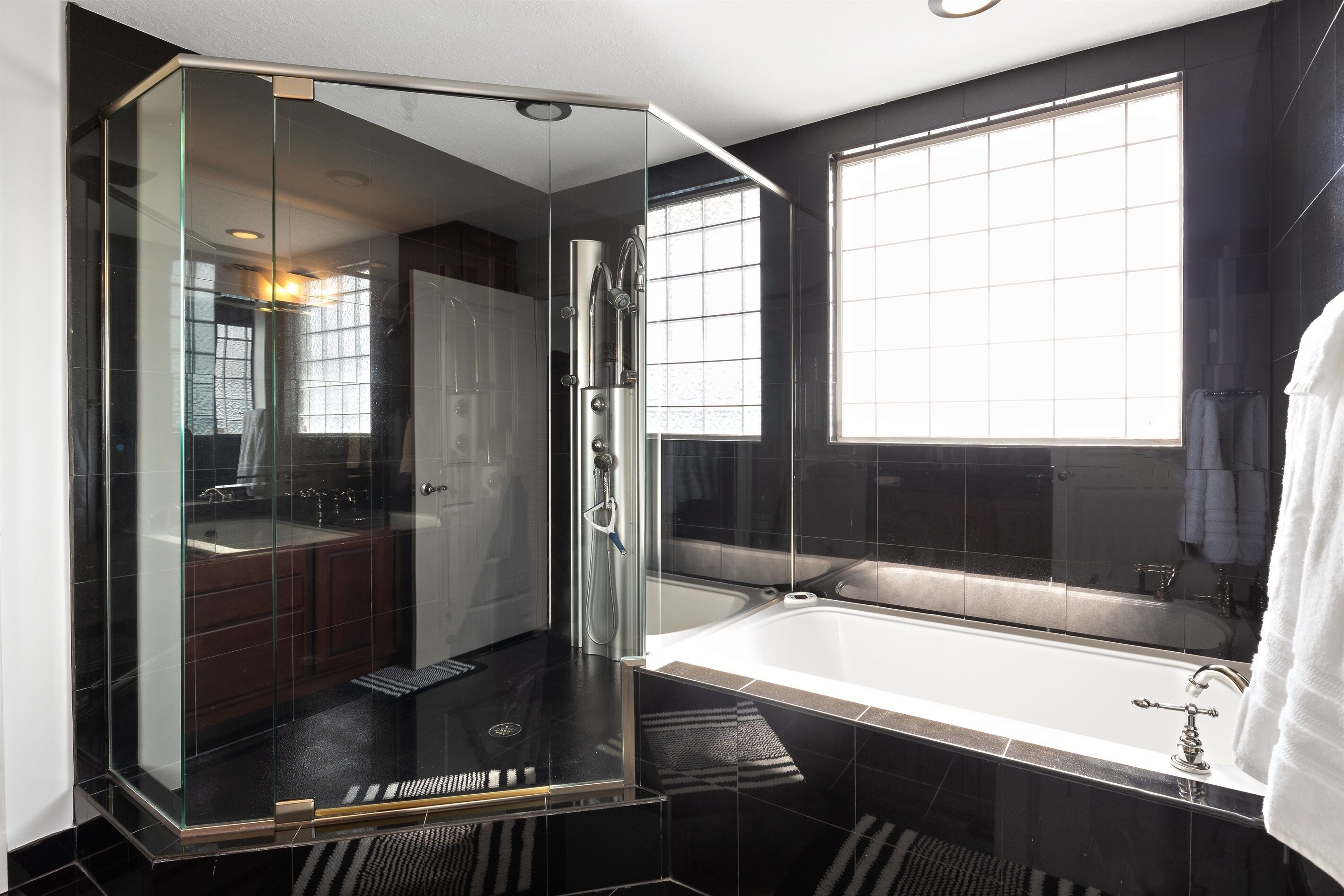 Une salle de bain moderne dotée d’une douche à parois de verre, d’une baignoire et d’une grande fenêtre laissant entrer la lumière naturelle.