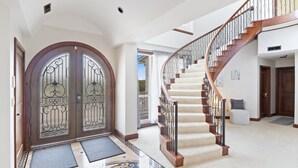 Une entrée imposante avec une double porte, un escalier recouvert de moquette et un sol carrelé.