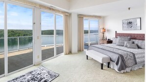 Une chambre spacieuse avec un grand lit, un banc et une vue sur un lac, visible à travers des portes-fenêtres coulissantes.