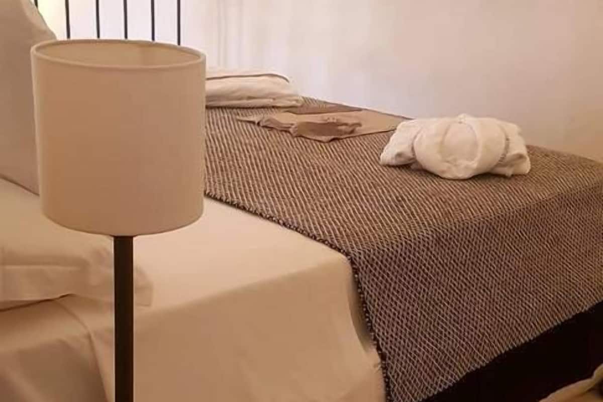 A neatly made bed with a white comforter and a brown blanket, a bedside lamp, and a TV mounted on the wall.