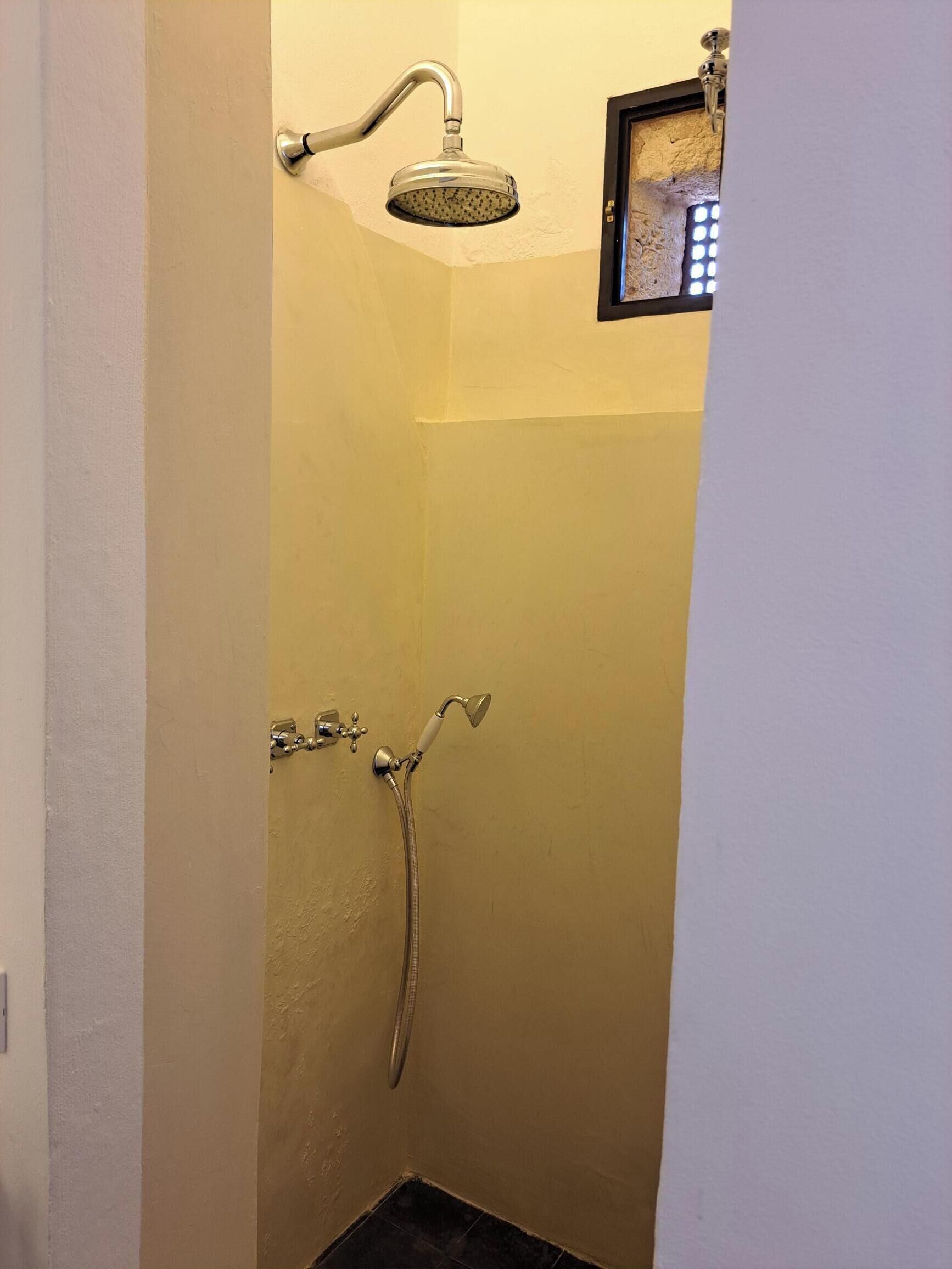 A small, enclosed shower area with a handheld showerhead and a wall-mounted faucet.