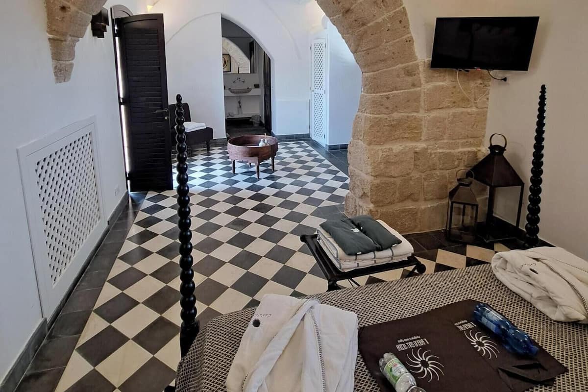 A hotel room with a checkered floor, a bed, a TV mounted on the wall, and a stone archway.