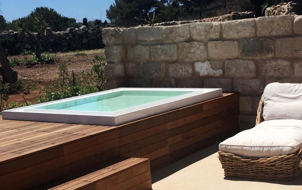 A rectangular hot tub on a wooden deck with a stone wall in the background.
