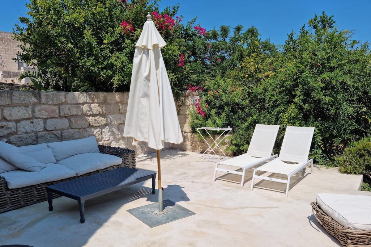 An outdoor seating area with a wicker sofa, two lounge chairs, a white umbrella, and a small table.