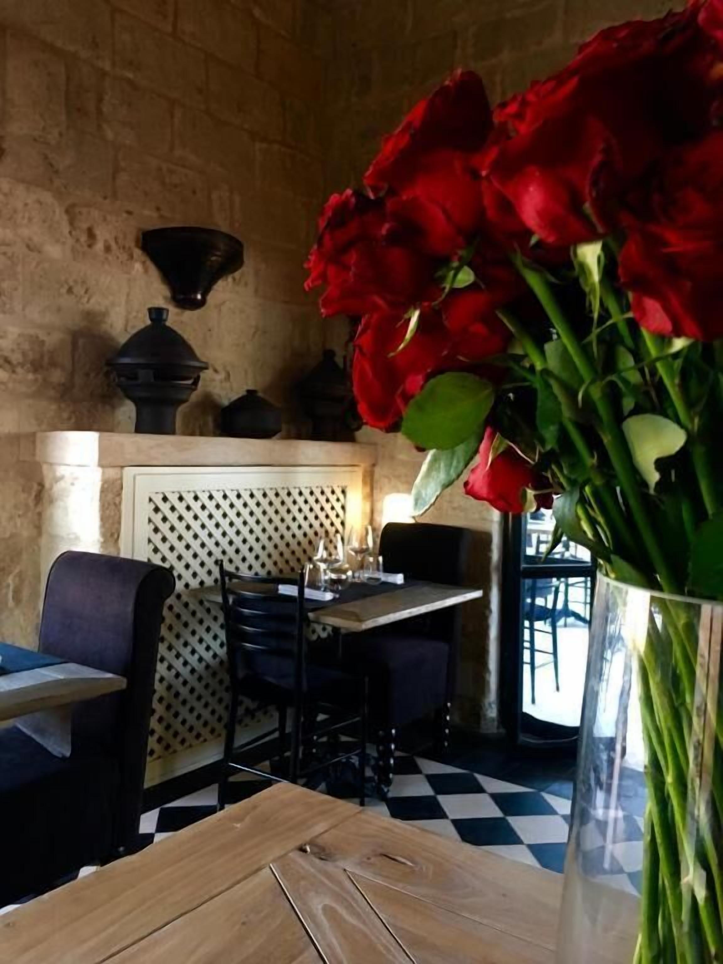 A dining area with a checkered floor, a table with chairs, and a vase of red flowers.