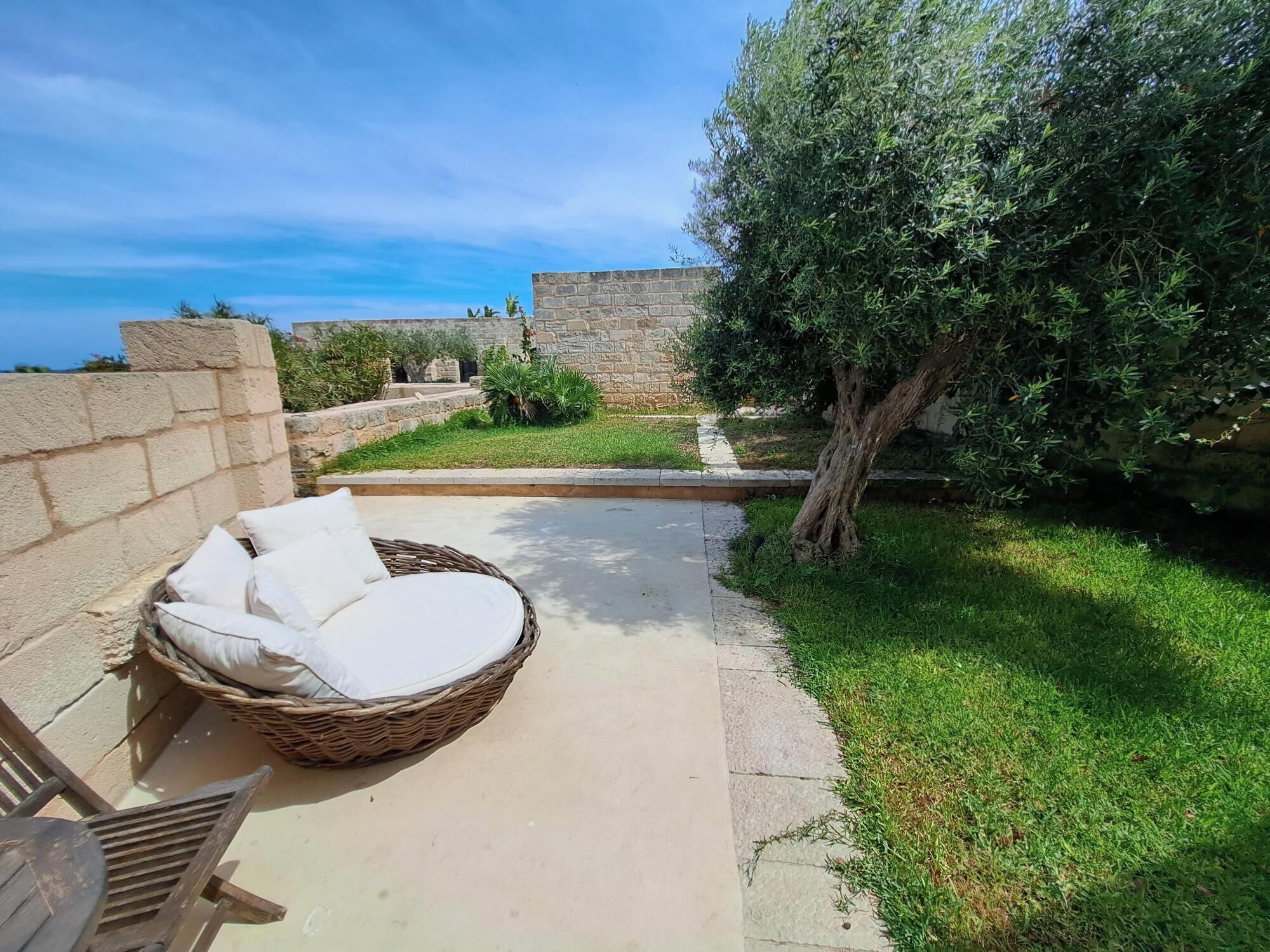 A wicker chair with cushions, a stone wall, and a grassy area with a tree.