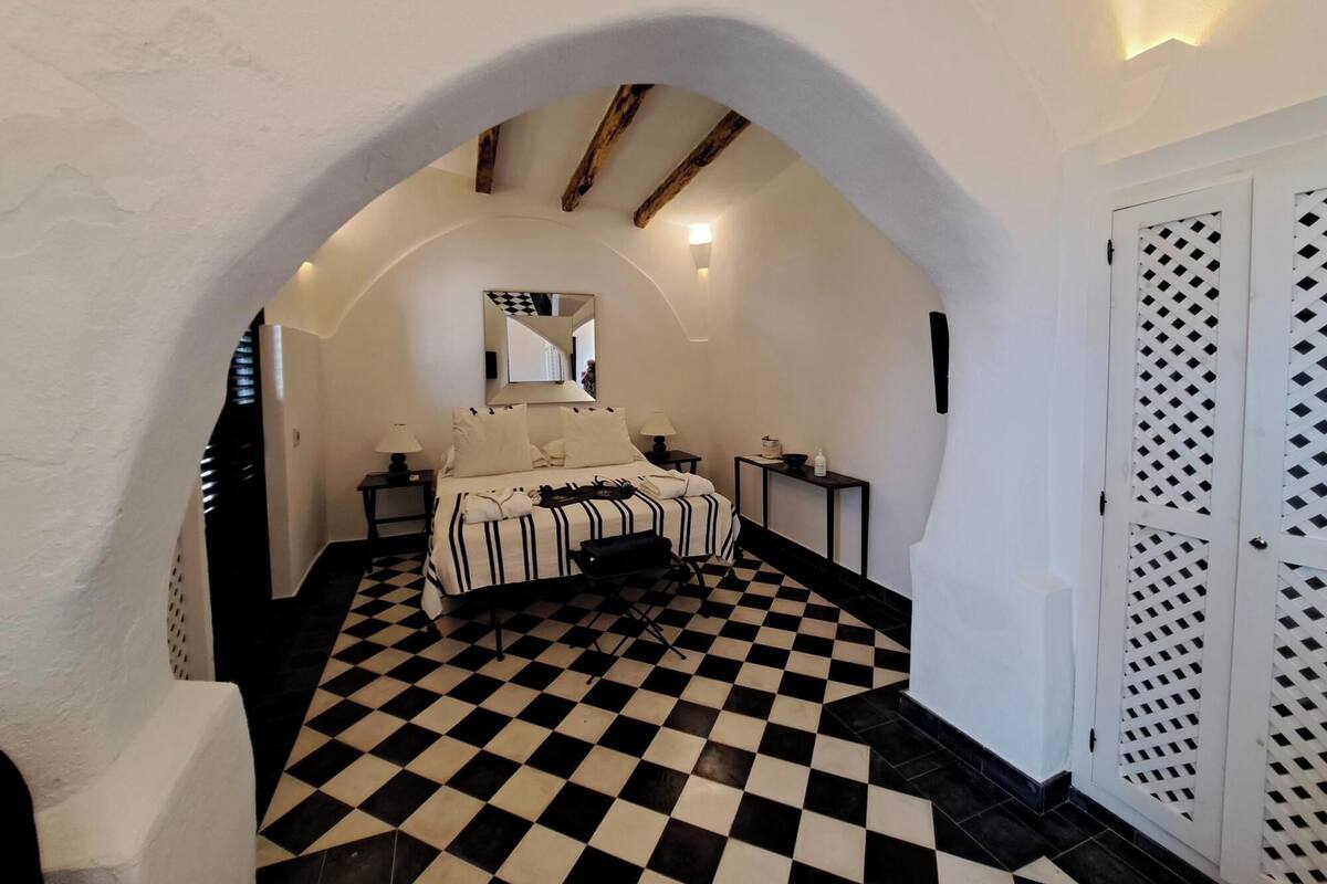 A bedroom with a checkered floor, a bed with striped bedding, a mirror, and a door with a lattice design.