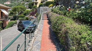 Un camino que sube por una ladera con un coche estacionado y un muro de piedra a un lado.