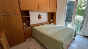 Un dormitorio con cama, armario de madera y escritorio pequeño con lámpara.