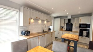 A modern kitchen with white cabinets, a wooden dining table, and a built-in oven.