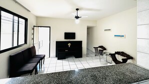 A modern living room with a black sofa, a TV on a black stand, a ceiling fan, and a large window.