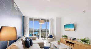 A modern living room with a sofa, a coffee table, a TV, and a view of a cityscape and water.