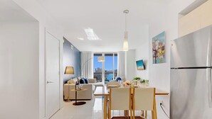 A modern living room with a sofa, dining table, and chairs. - Pool + Infinity View w/ Balcony + Gym (Hallandale Beach)