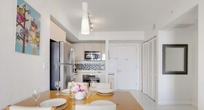 Una cucina moderna con elettrodomestici in acciaio inossidabile, un'area pranzo con un tavolo in legno e sedie bianche, e un quadro colorato appeso al muro.