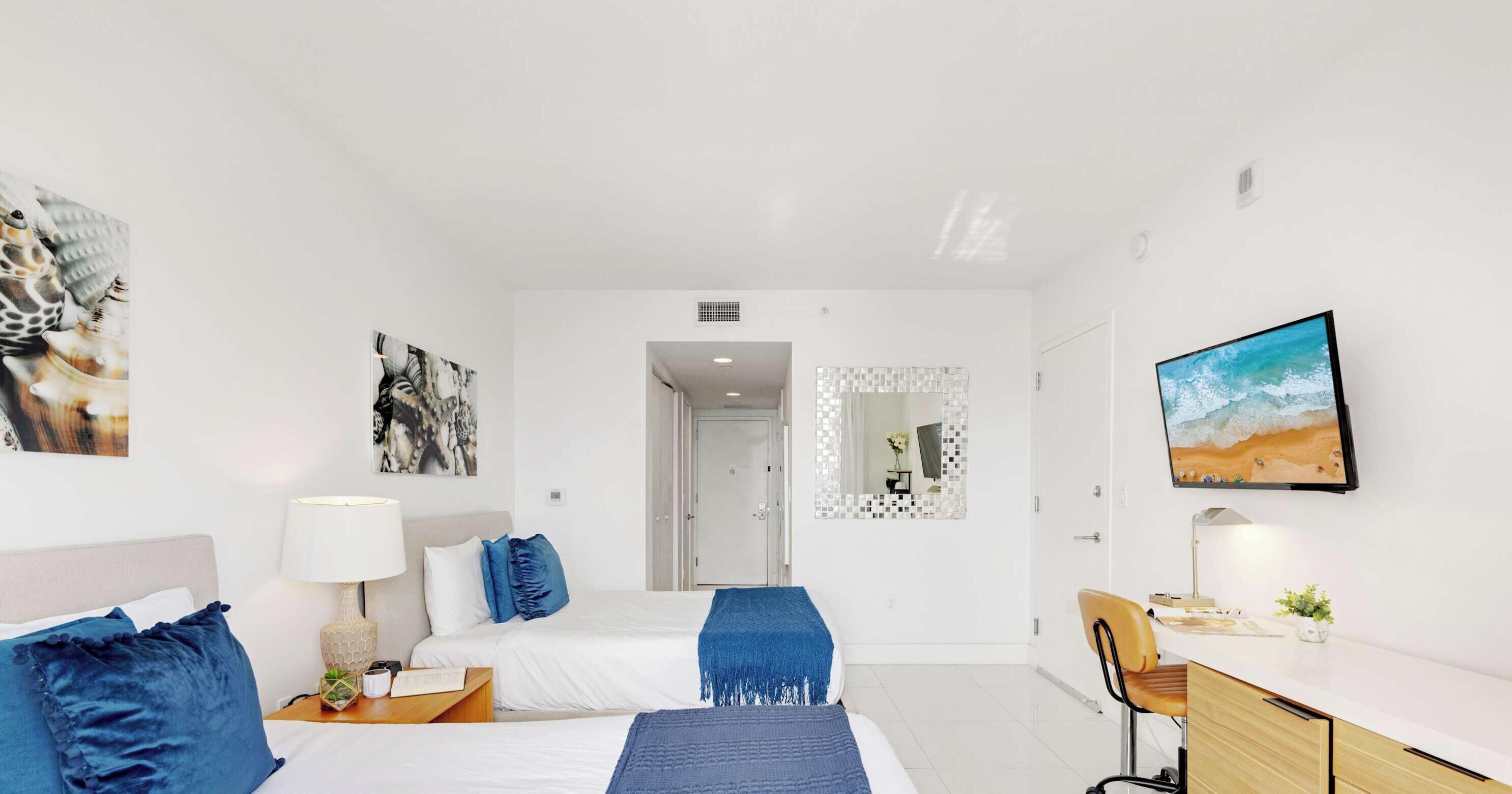 Una habitación de hotel moderna con dos camas, un escritorio, una silla y obras de arte en las paredes.