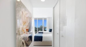 A modern hotel room with a large window, a bed with a blue blanket, and a white wardrobe.