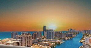 A coastal cityscape with high-rise buildings, a marina, and a sunset. - Infinite View Balcony|Studio Resort (Hallandale Beach)