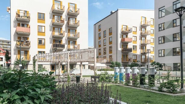 Un edificio residencial con varios balcones, entrada protegida por un portón y un jardín bien cuidado.