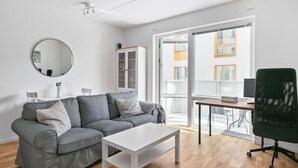 Una sala de estar moderna con un sofá gris, una mesa de centro blanca, una silla de oficina negra, un espejo redondo y un armario.