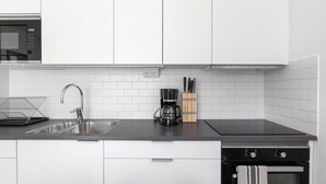 Una cocina moderna con armarios blancos, un lavamanos de acero inoxidable, una cafetera y un lavavajillas.