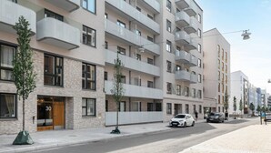 Un edificio residencial de varios pisos con balcones, entrada a nivel de calle y zona de estacionamiento.