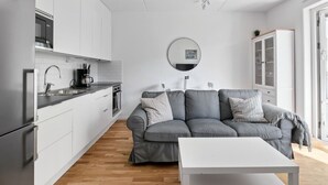 Una cocina moderna con armarios blancos, un sofá gris y una mesa blanca.