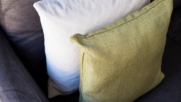 A close-up of a grey sofa with a white and a green pillow. - The Whitecross Street Collection (London)