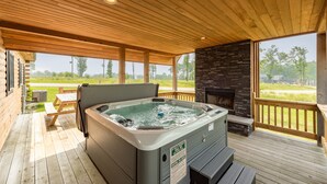 A wooden deck with a hot tub, stone fireplace, and a view of the outdoors. - Dog Friendly Mountain Lodge w/ Hot Tub (McHenry)