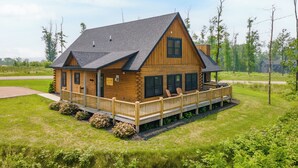 A wooden cabin with a porch and deck, surrounded by greenery. - Dog Friendly Mountain Lodge w/ Hot Tub (McHenry)