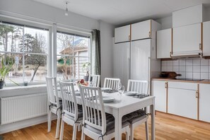 Eine moderne Küche mit weißen Schränken, einem Esstisch für vier Personen und Blick ins Freie durch große Fenster.