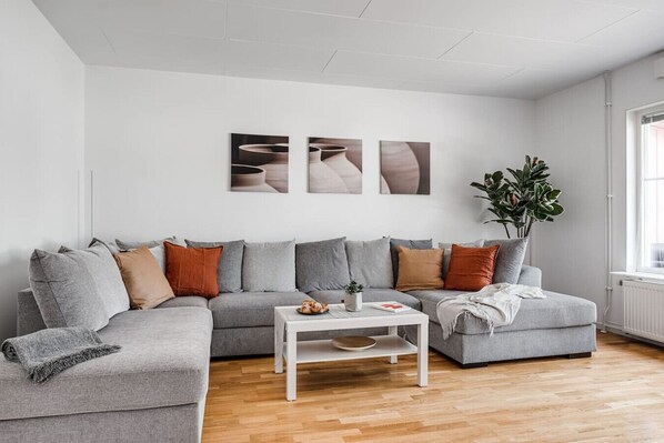 Ein modernes Wohnzimmer mit einer grauen Eckcouch, einem weißen Couchtisch und einem großen Fenster.