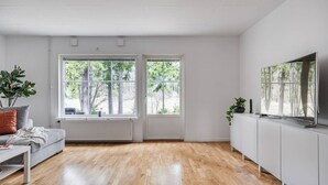 A modern living room with a sofa, a TV, and a large window with a view of trees.