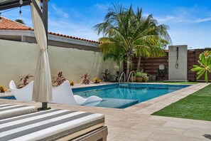A swimming pool with a tiled deck, lounge chairs, and potted plants.