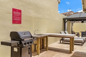 Eine Terrasse im Freien mit Grill, Tisch und Liegestühlen.