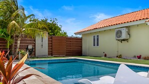 Una piscina con recinzione in legno, una casa con tetto in tegole e uno scaldabagno montato a parete.