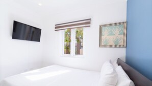 Una camera da letto con un letto, una TV a parete, una finestra con persiane e un quadro appeso al muro.