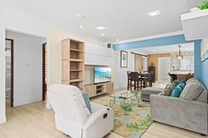 A modern living room with a sofa, a glass coffee table, and a TV. There is a dining area with a table and chairs. - 3-BR Private Pool Paradise - BBQ Grill - Gazebo (Oranjestad)