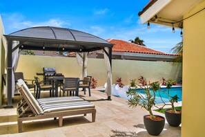 Ein überdachter Außenbereich mit Pool, Liegestühlen und Grill.