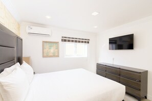 Ein Schlafzimmer mit Bett, Kommode, Flachbildfernseher und Klimaanlage.