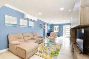 Ein Wohnzimmer mit einem beigen Sofa, einem Glastisch und einem Flachbildfernseher.