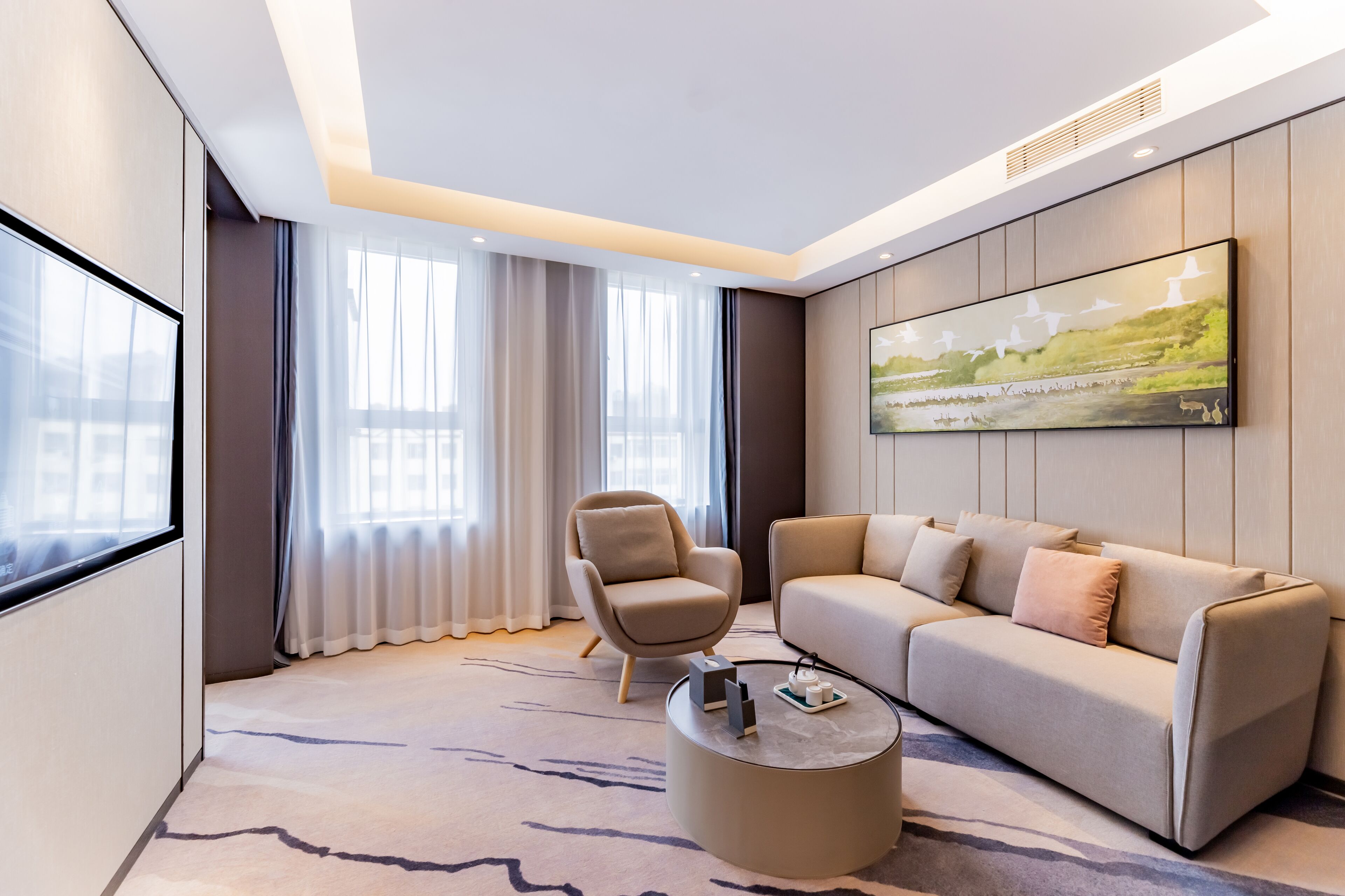 A modern living room with a beige sofa, a round coffee table, and a large painting on the wall.