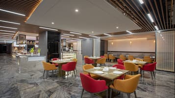Restaurante moderno com chão de mármore, cadeiras vermelhas e amarelas, e um balcão exibindo diversos alimentos.