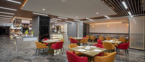 Un restaurante moderno con suelo de mármol, sillas rojas y amarillas, y una barra con exhibición de alimentos.