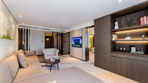 Una sala de estar moderna con sofá, sillón y mesa de centro. Hay un televisor montado en la pared y una estantería con objetos decorativos.