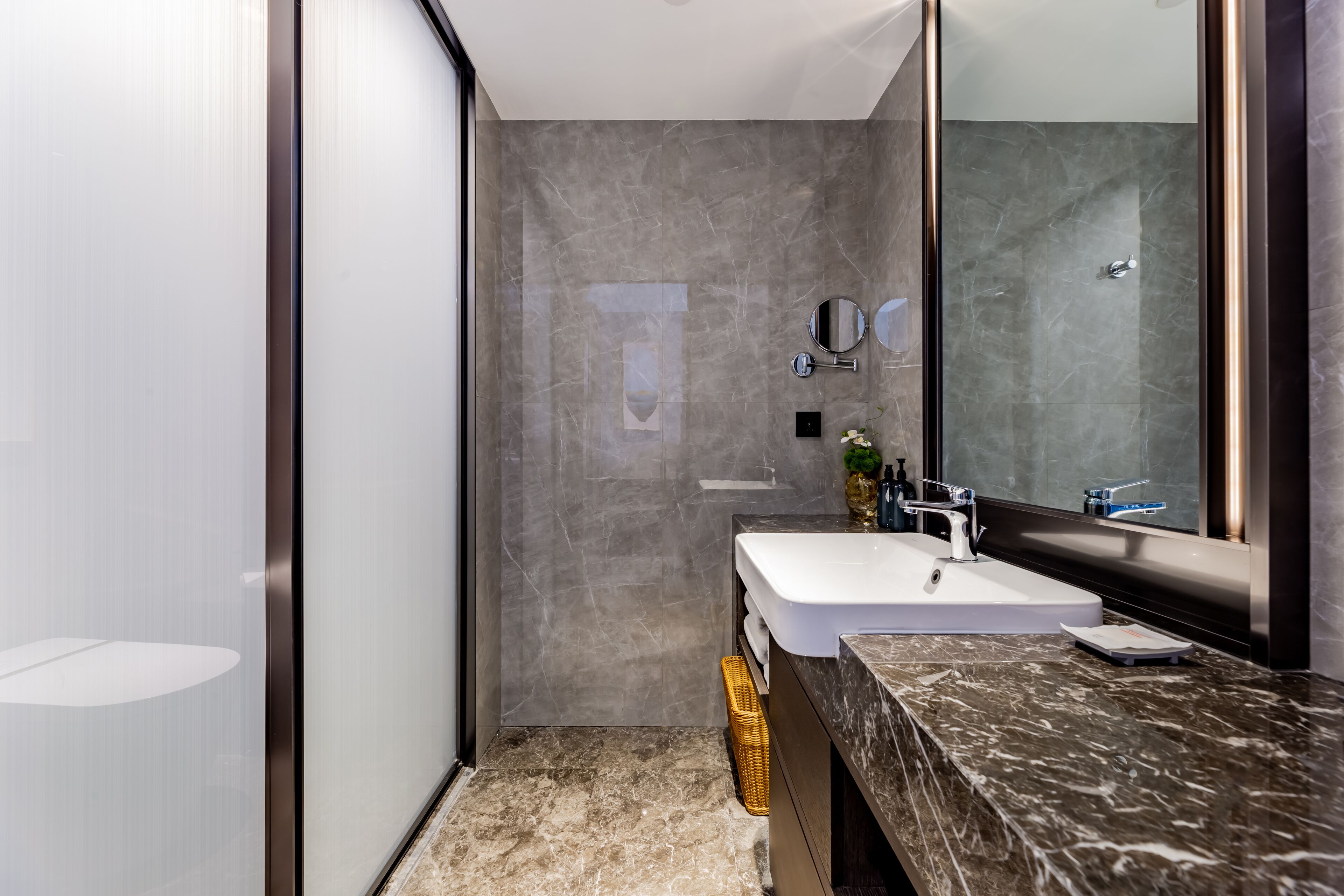 Un baño moderno con un espejo grande, un lavabo blanco y una encimera de mármol.