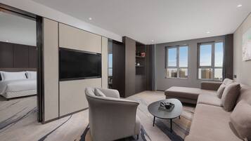 A modern hotel room with a large bed, a sofa, a coffee table, and a TV.