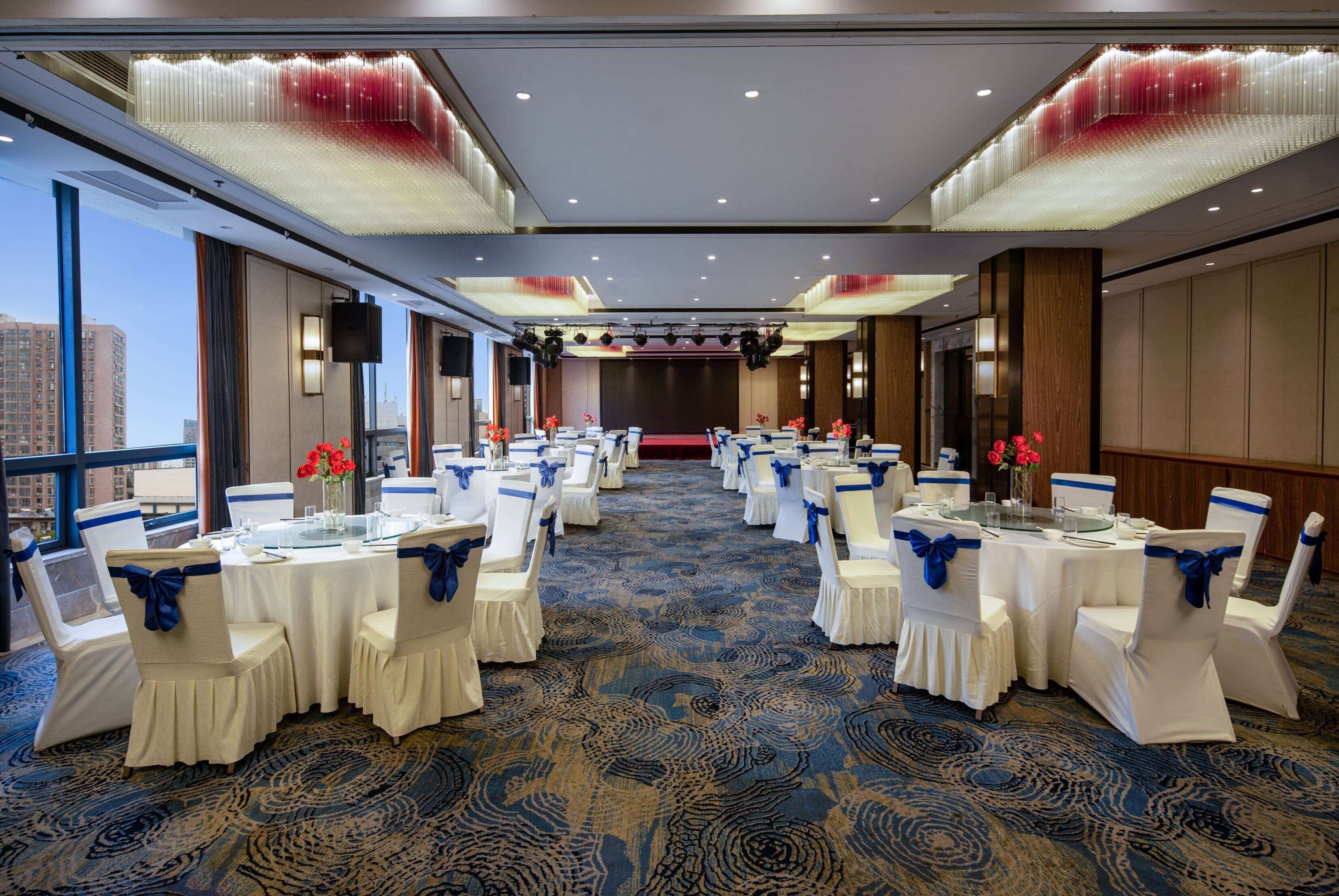 Un salón de conferencias con mesas y sillas blancas, cintas azules y una alfombra estampada.