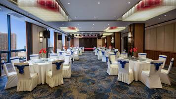 Un salón de conferencias con mesas y sillas blancas, cintas azules y una alfombra estampada.