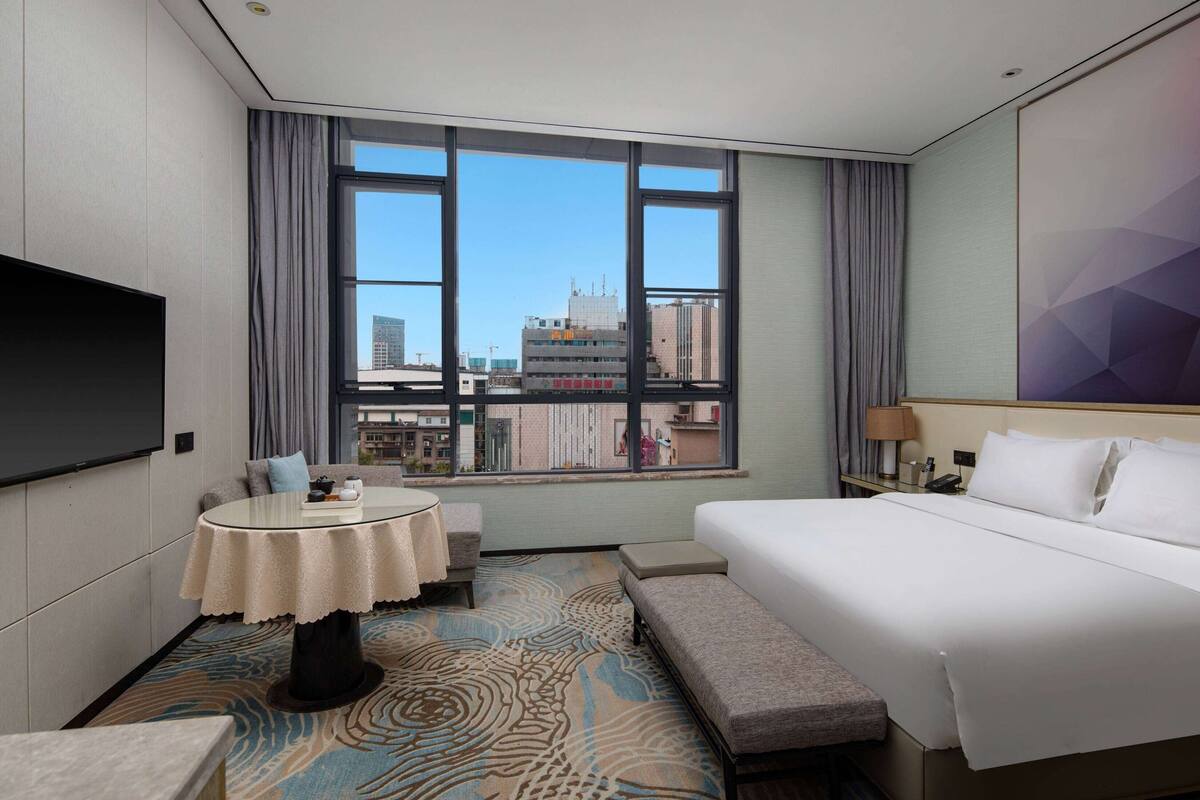 A hotel room with a large bed, a round table, a sofa, and a TV.